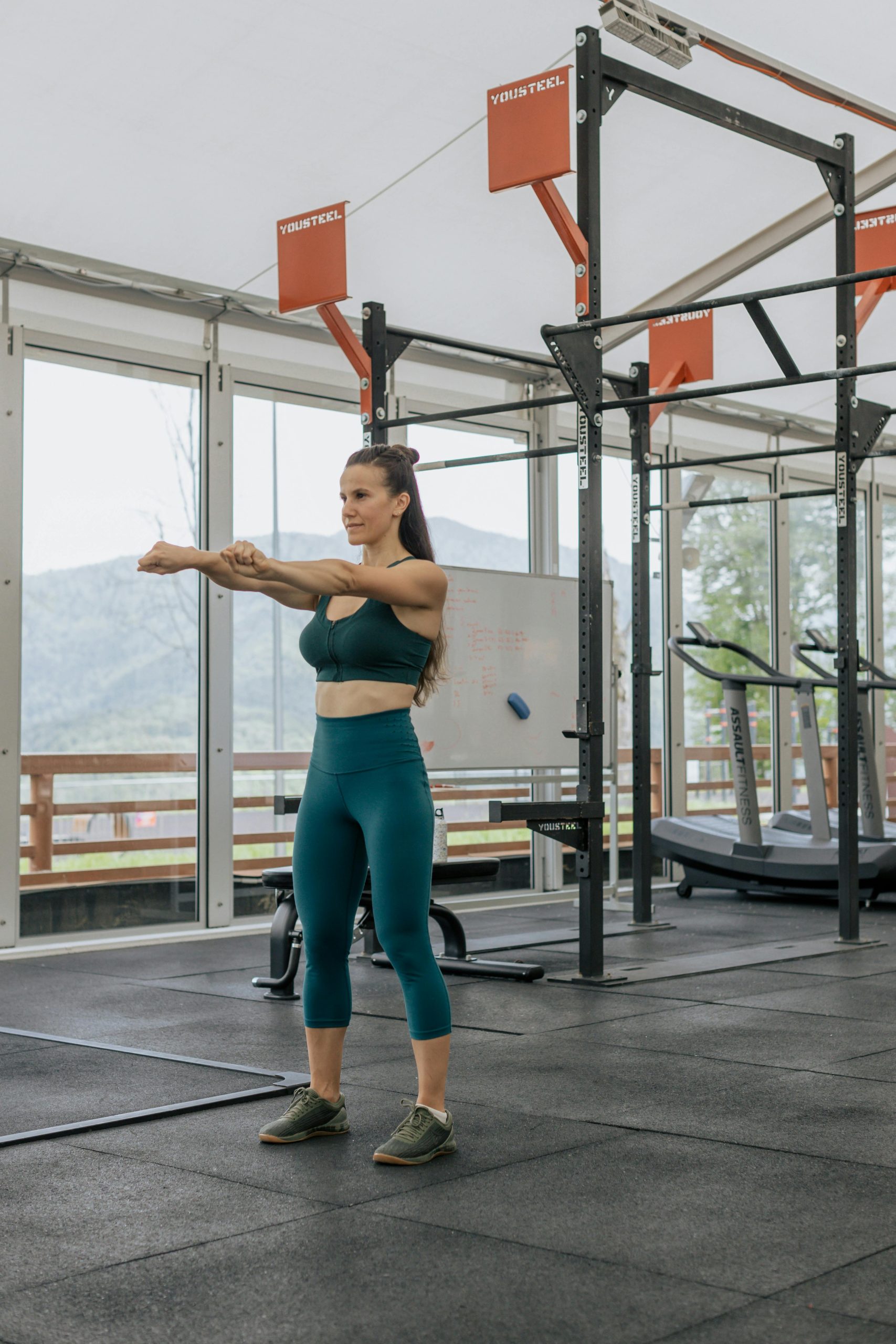 Une femme en tenue sportive s'étire dans une salle de sport moderne avec une vue panoramique à l'extérieur.