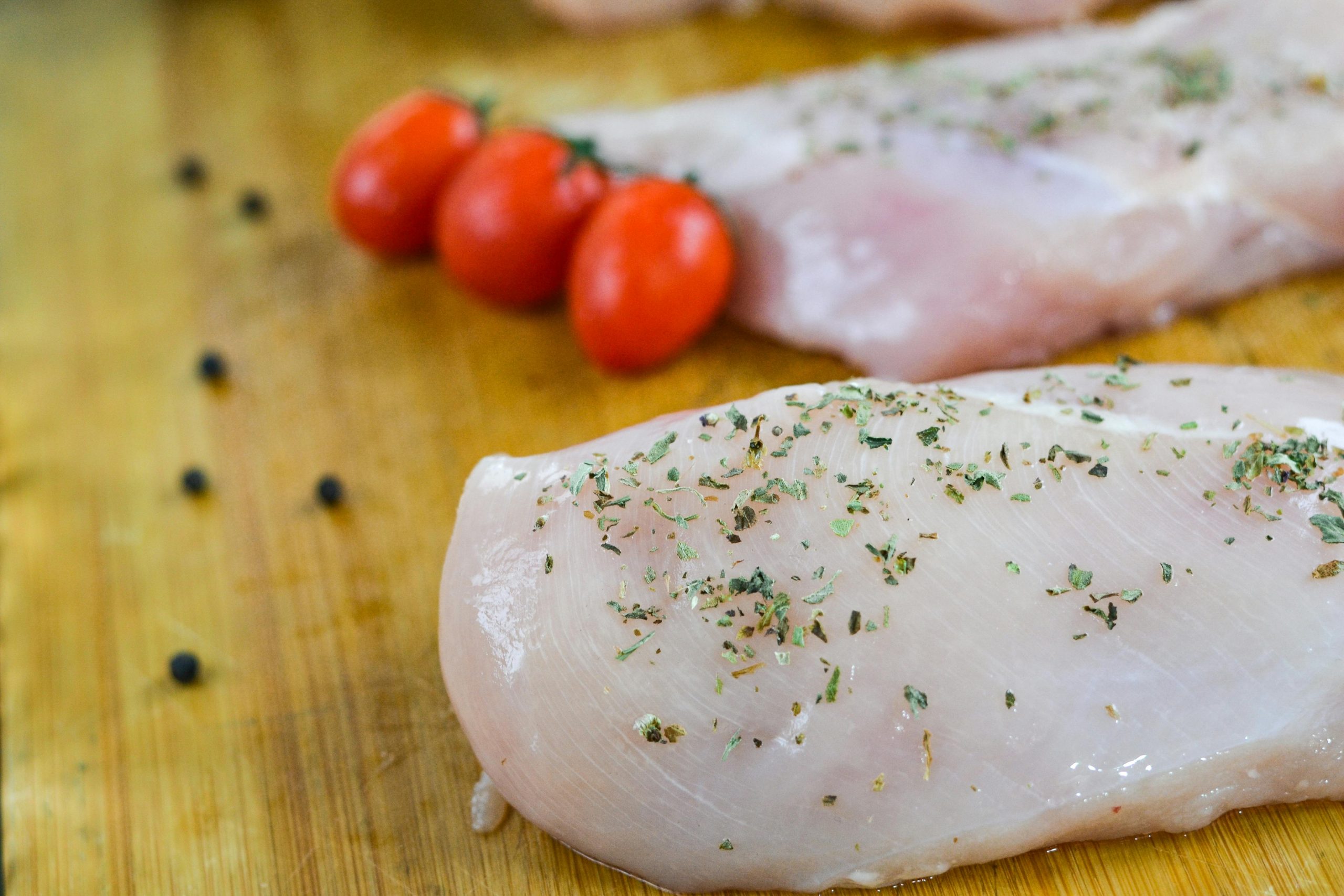 Poulet frais non cuit saupoudré d'herbes, accompagné de tomates cerises sur une planche en bois.