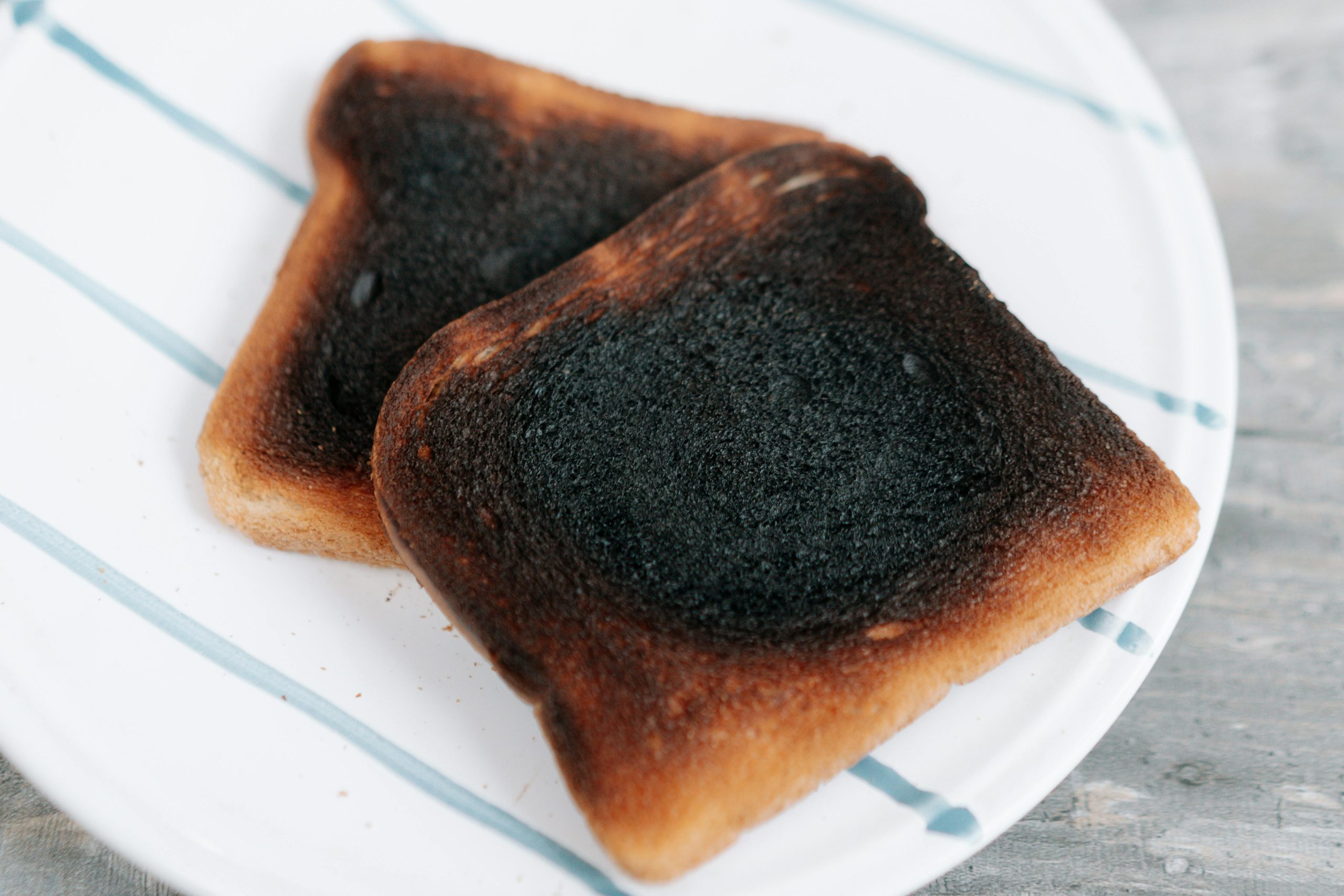 Two slices of burnt toast served on a white ceramic plate, perfect for breakfast or food concepts. Deux tranches de pain grillé brûlé servies sur une assiette en céramique blanche, parfaites pour le petit-déjeuner ou des concepts culinaires.