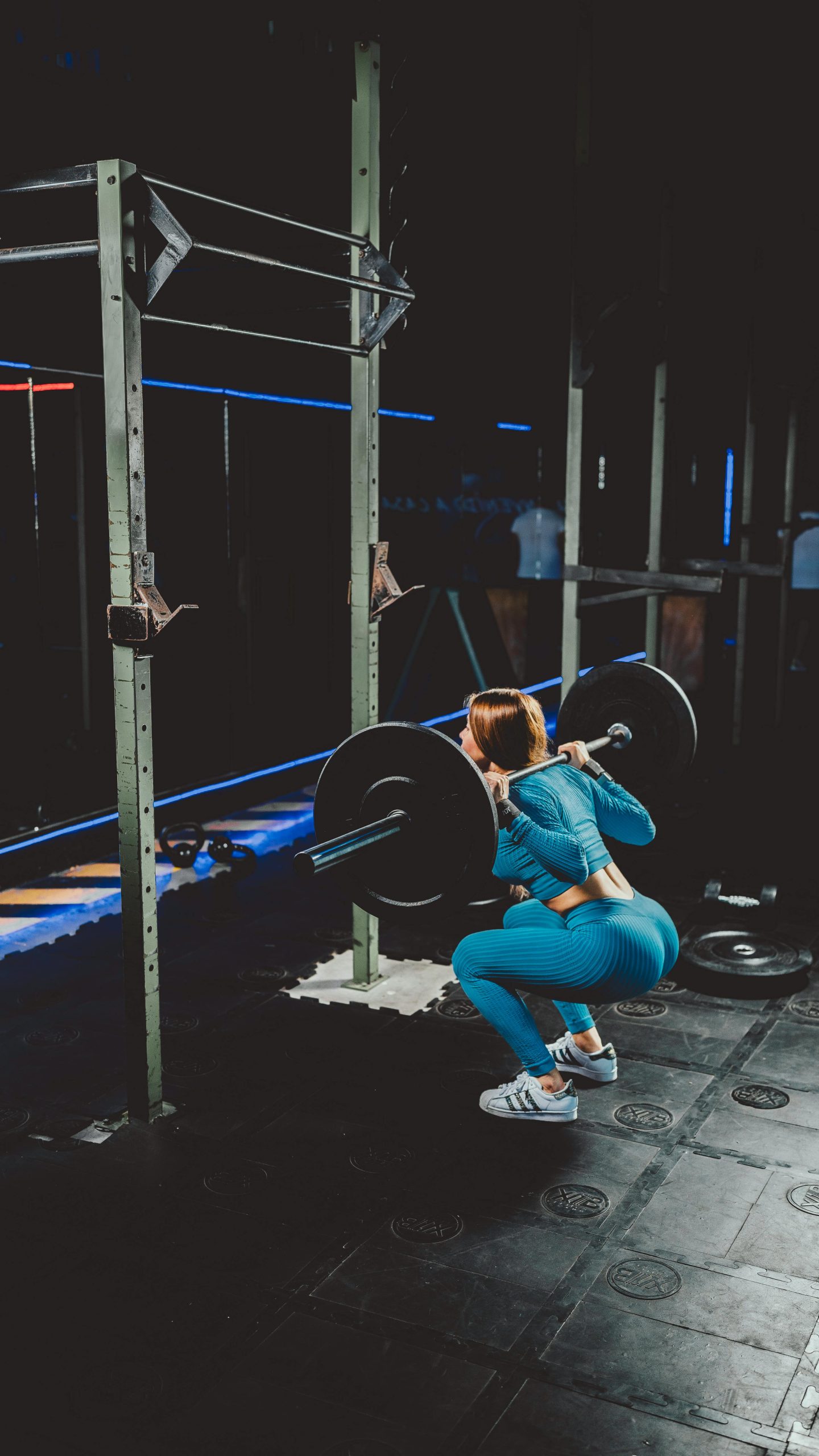 Woman squatting avec une barre de musculation dans une salle de sport, mettant en avant la force et la concentration sur la forme physique.