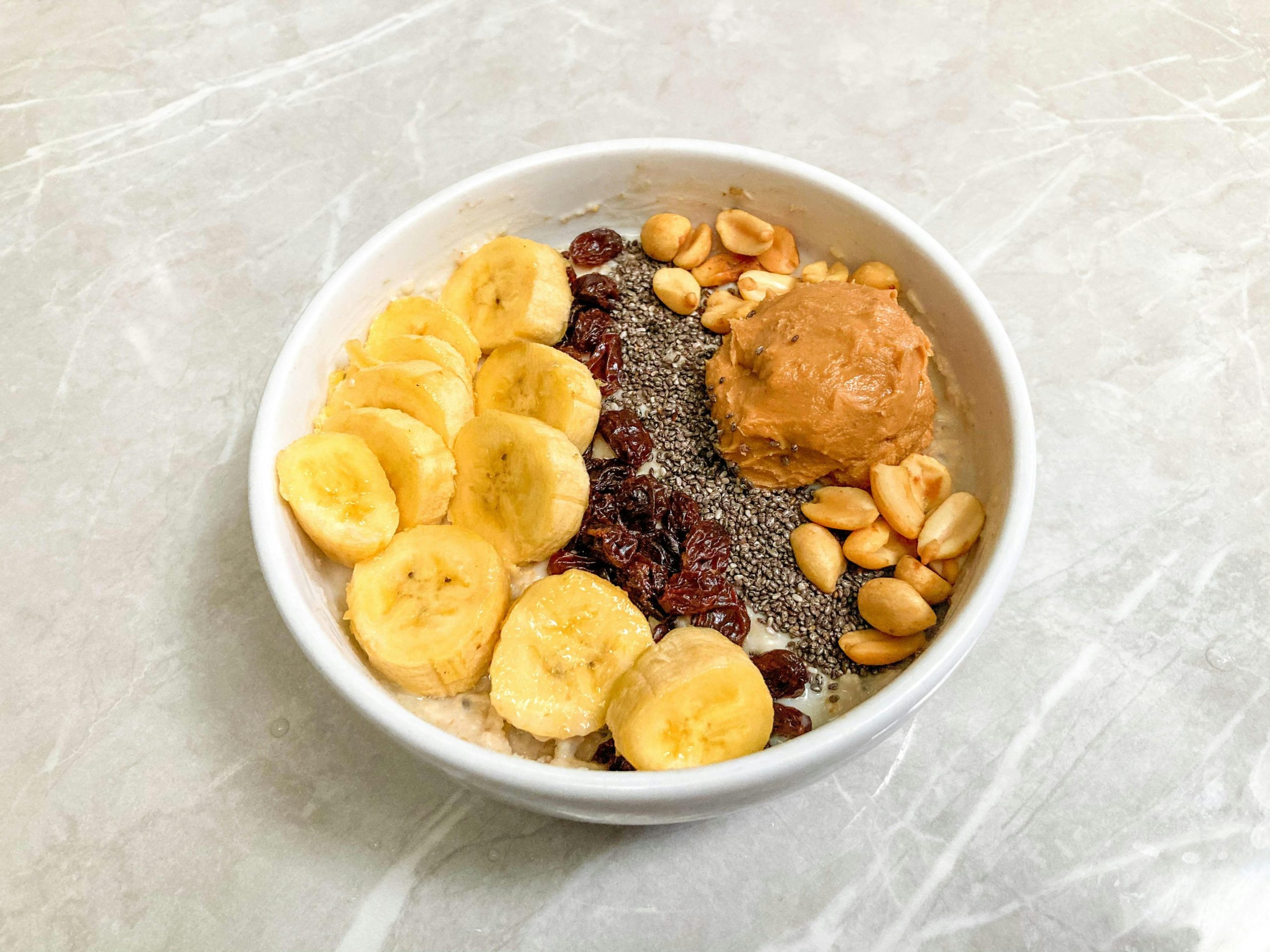 Un bol de petit-déjeuner délicieux avec bananes, graines de chia, cacahuètes, raisins secs et beurre de cacahuète.