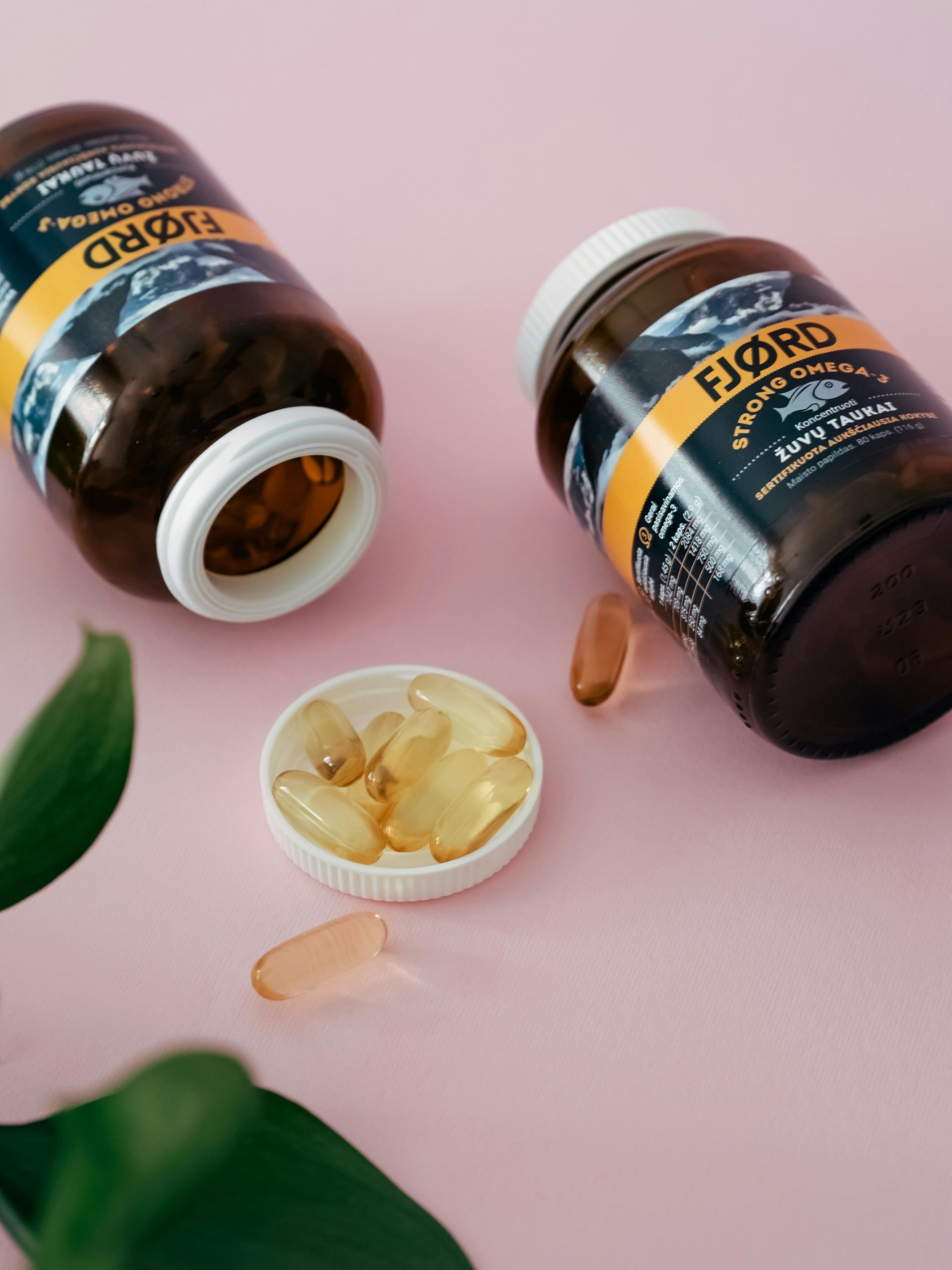 Close-up de bouteilles et capsules de complément en oméga 3 sur une surface rose.