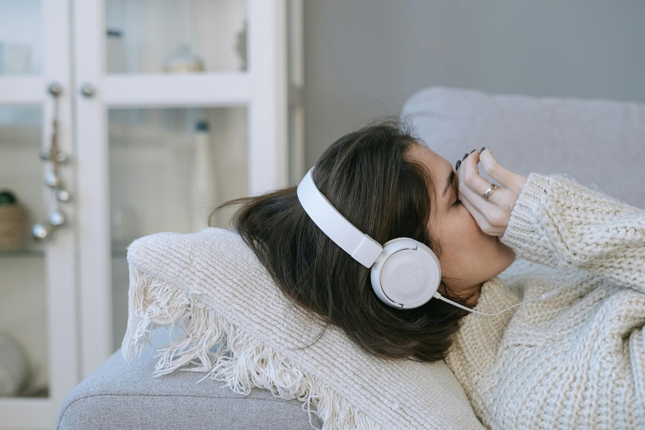 Woman allongée sur un canapé avec des écouteurs, paraissant détendue ou pensive à l'intérieur, ambiance cosy.