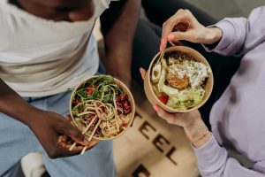 Two people holding bowls filled with salad and pasta, emphasizing healthy lifestyle choices. Deux personnes tenant des bols remplis de salade et de pâtes, mettant en avant des choix de vie sains.