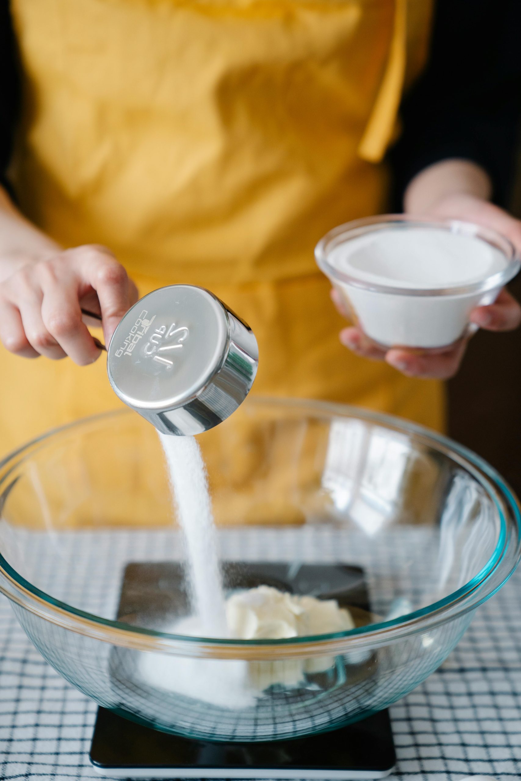 Personne versant du sucre d'une tasse à mesurer dans un bol, prête pour la pâtisserie.