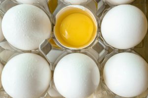 A high-angle view of fresh eggs in a carton with one cracked open showing the yolk. Une vue de haut d'œufs frais dans un carton avec un œuf cassé montrant le jaune.