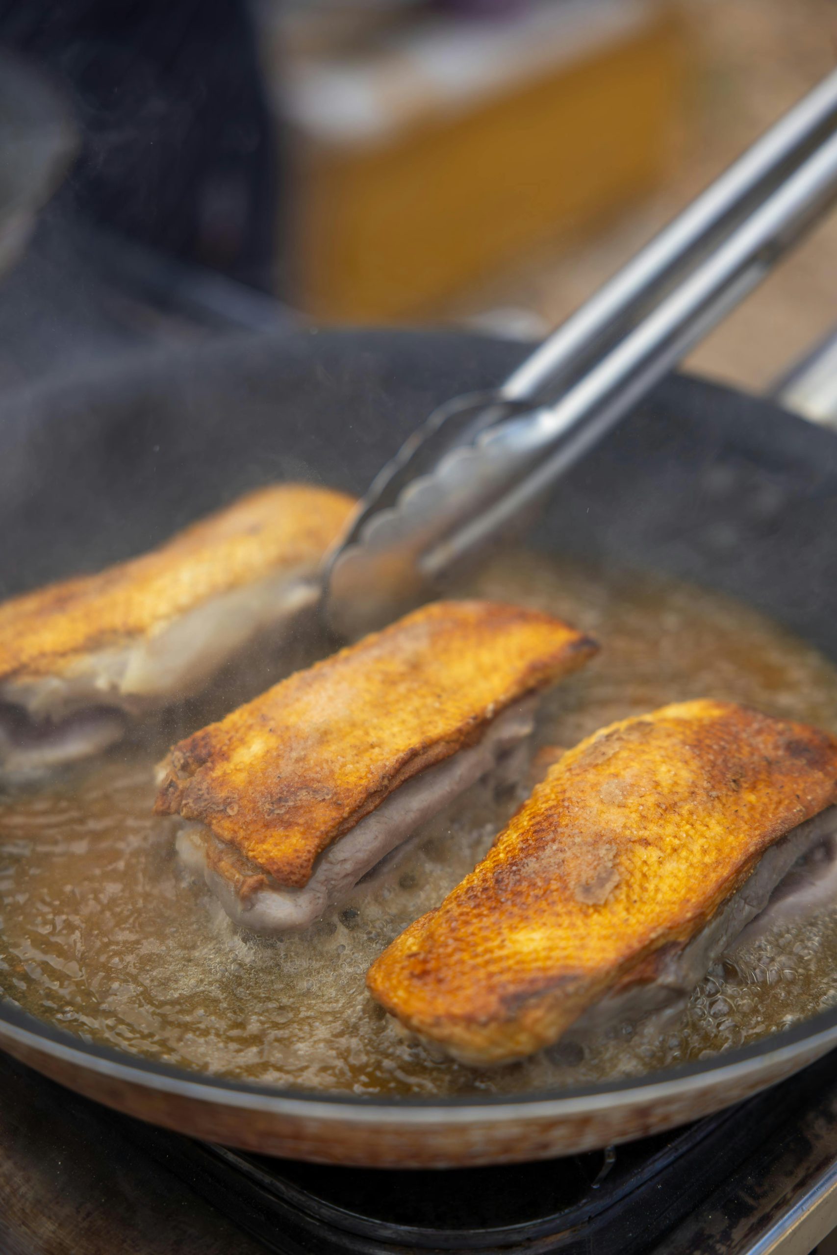 Saisissantes poitrines de canard cuites à la perfection dans une poêle à frire avec des pinces.