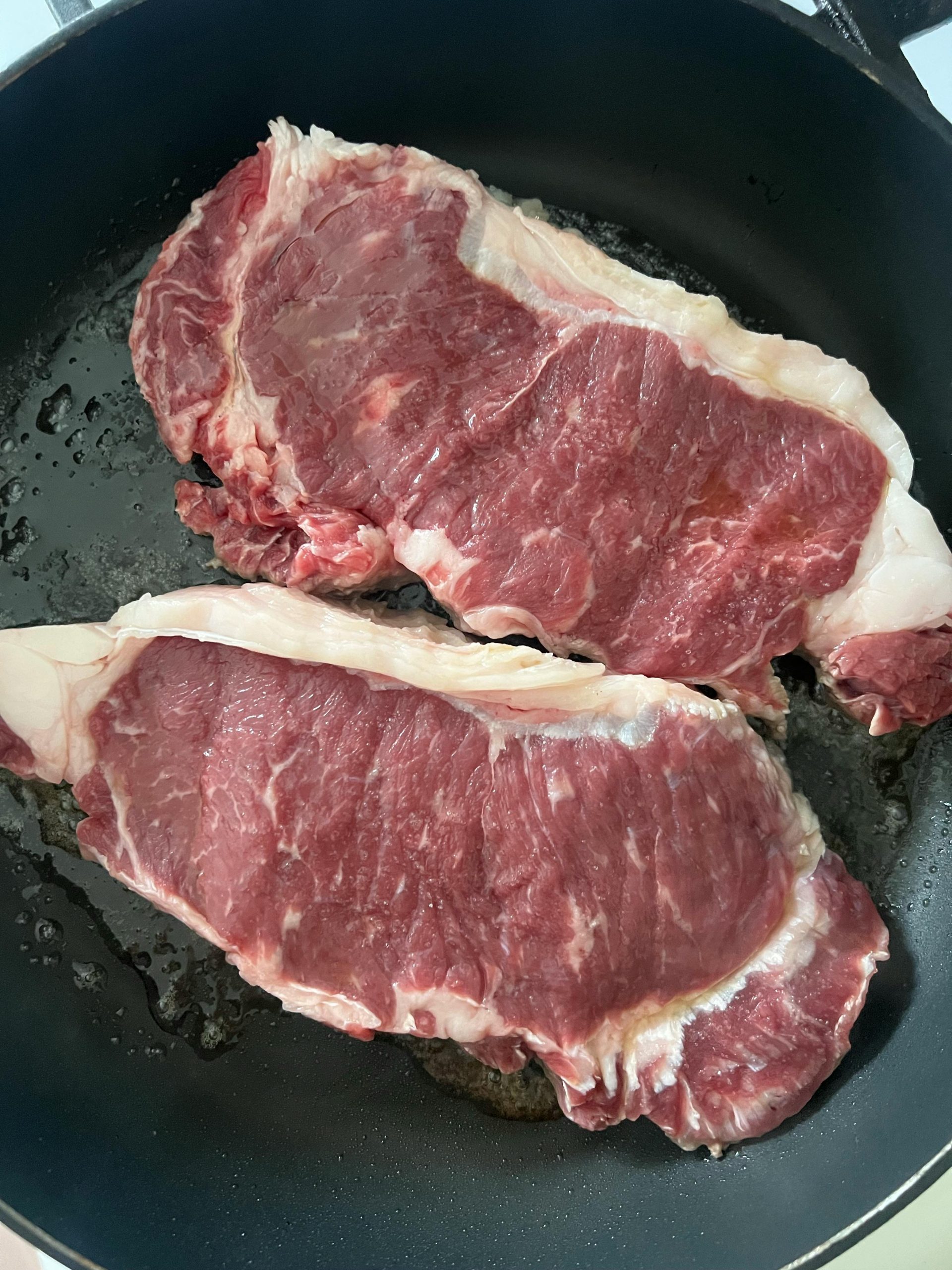 Two raw ribeye steaks in a frying pan, ready to be cooked. Deux steaks de faux-filet crus dans une poêle à frire, prêts à être cuisinés.