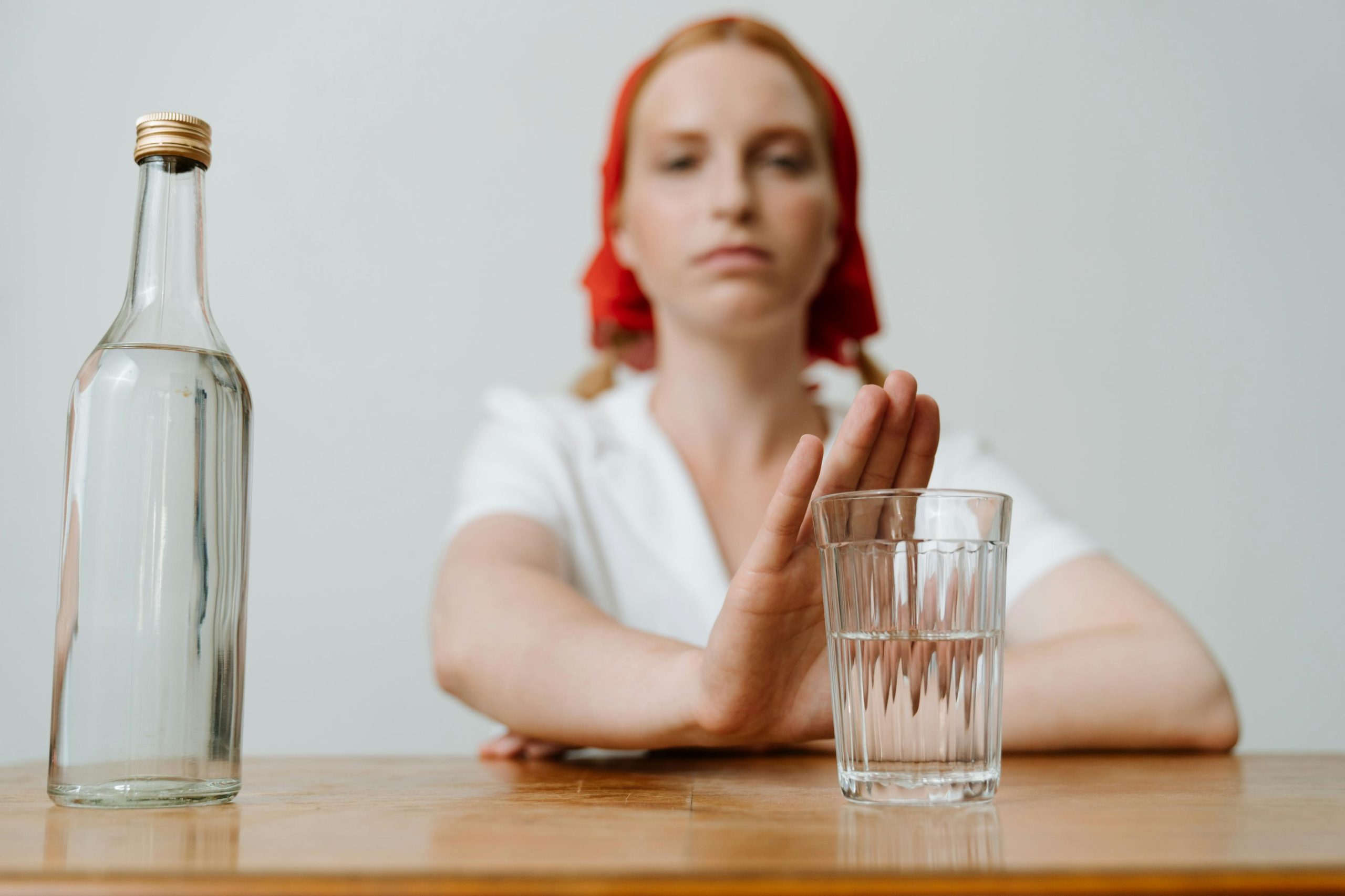 A woman with a red kerchief rejects a glass of alcohol, symbolizing sobriety or refusal. Une femme avec un foulard rouge refuse un verre d'alcool, symbolisant la sobriété ou le refus.