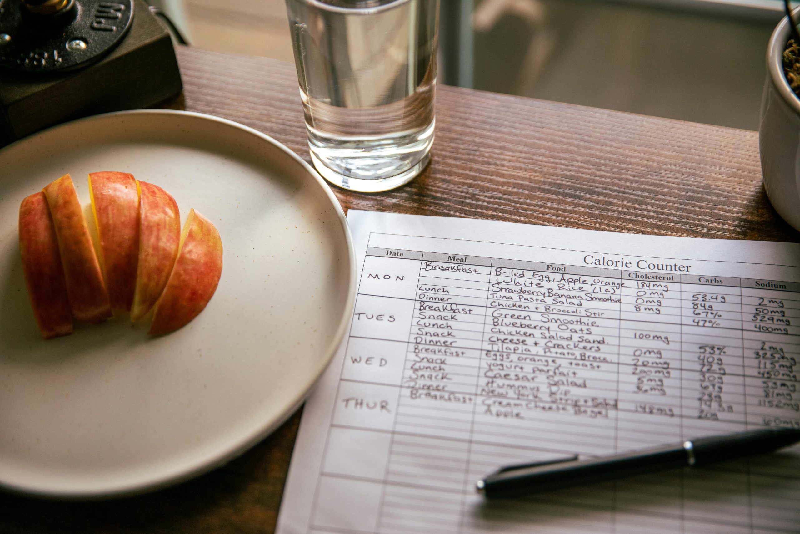 Une table dressée avec des tranches de pomme, une feuille de comptage de calories et un verre d'eau pour une scène de régime.