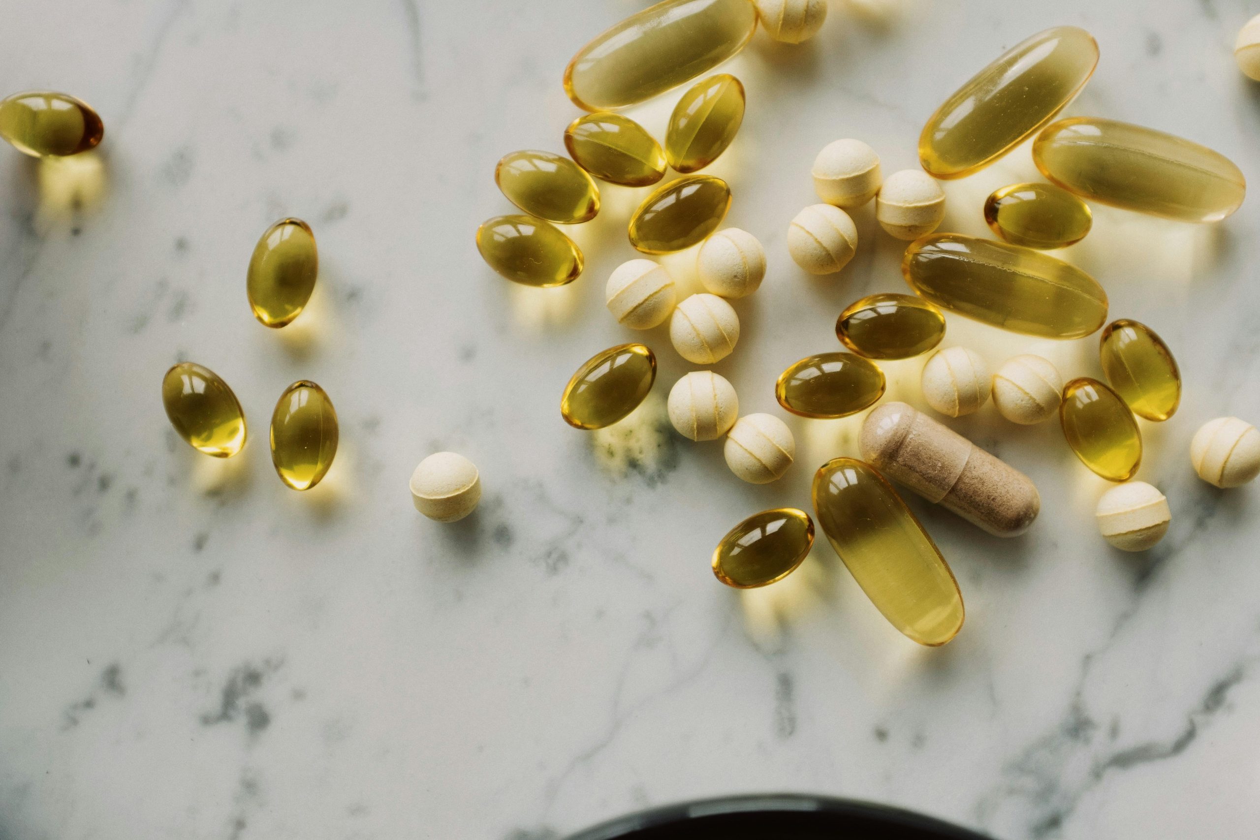 Variety of supplements and capsules scattered on a marble surface, suitable for healthcare themes. Variété de compléments alimentaires et de gélules éparpillés sur une surface en marbre, adaptée aux thèmes de santé.