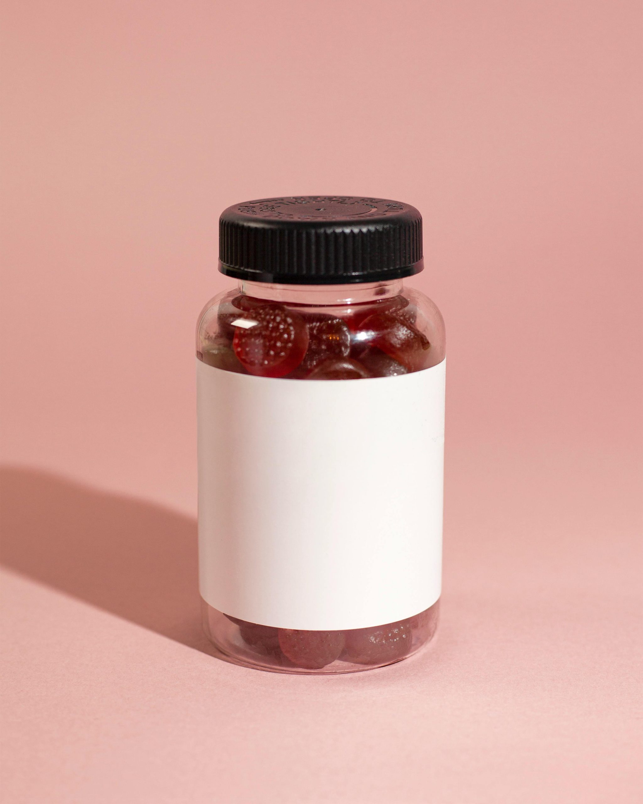 Clear bottle avec des vitamines gélifiées rouges sur un fond rose, mettant en avant la simplicité du produit.