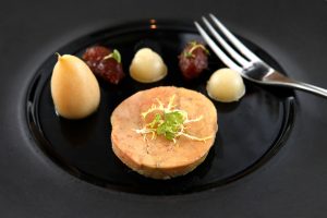 Delicate foie gras served on a black ceramic plate with garnish and puree accompaniments. Foie gras délicat servi sur une assiette en céramique noire avec garniture et accompagnements de purée.