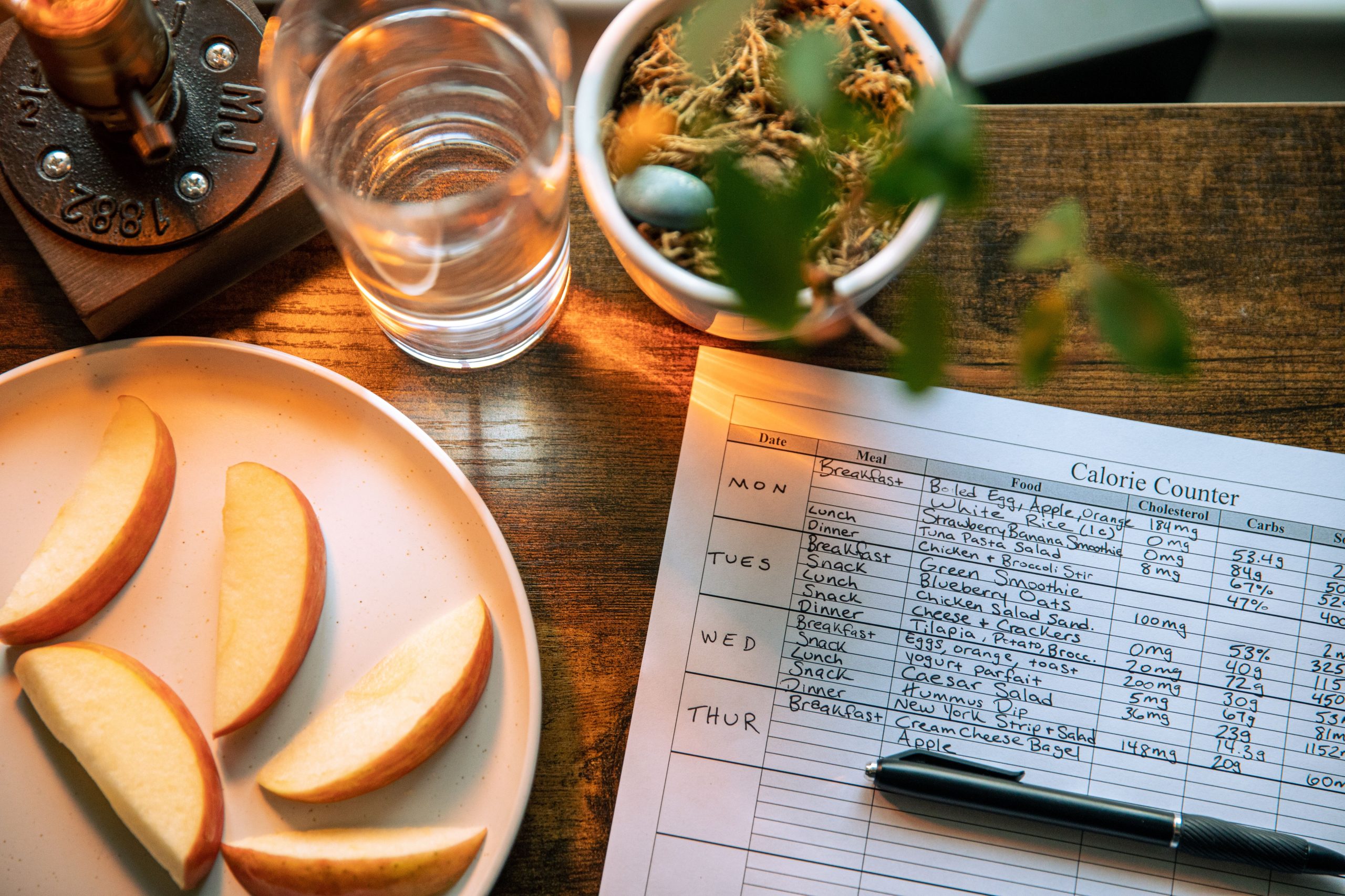 Top view of apple slices, water, and a calorie counter sheet on a wooden table promoting a healthy lifestyle. Vue de dessus de tranches de pomme, d'eau et d'une feuille de comptage des calories sur une table en bois promouvant un mode de vie sain.