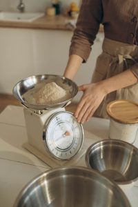 A woman weighing flour using a kitchen scale, preparing for baking in a cozy kitchen setting. Une femme pesant de la farine à l'aide d'une balance de cuisine, se préparant à la cuisson dans un cadre de cuisine confortable.