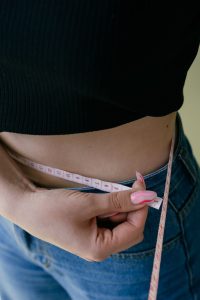 A woman measures her waist with a tape measure, focusing on fitness and weight management. Une femme mesure sa taille avec un mètre ruban, en se concentrant sur la forme physique et la gestion du poids.