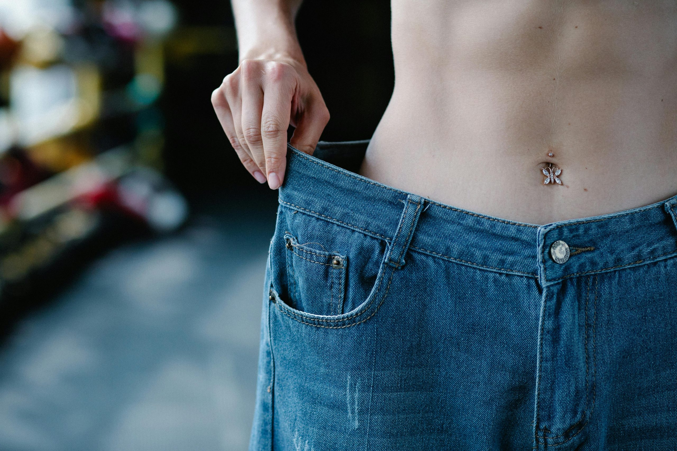 Close-up view of a slim waist and loose jeans representing weight loss or fitness progress. Vue rapprochée d'une taille fine et d'un jean ample représentant une perte de poids ou une progression en fitness.