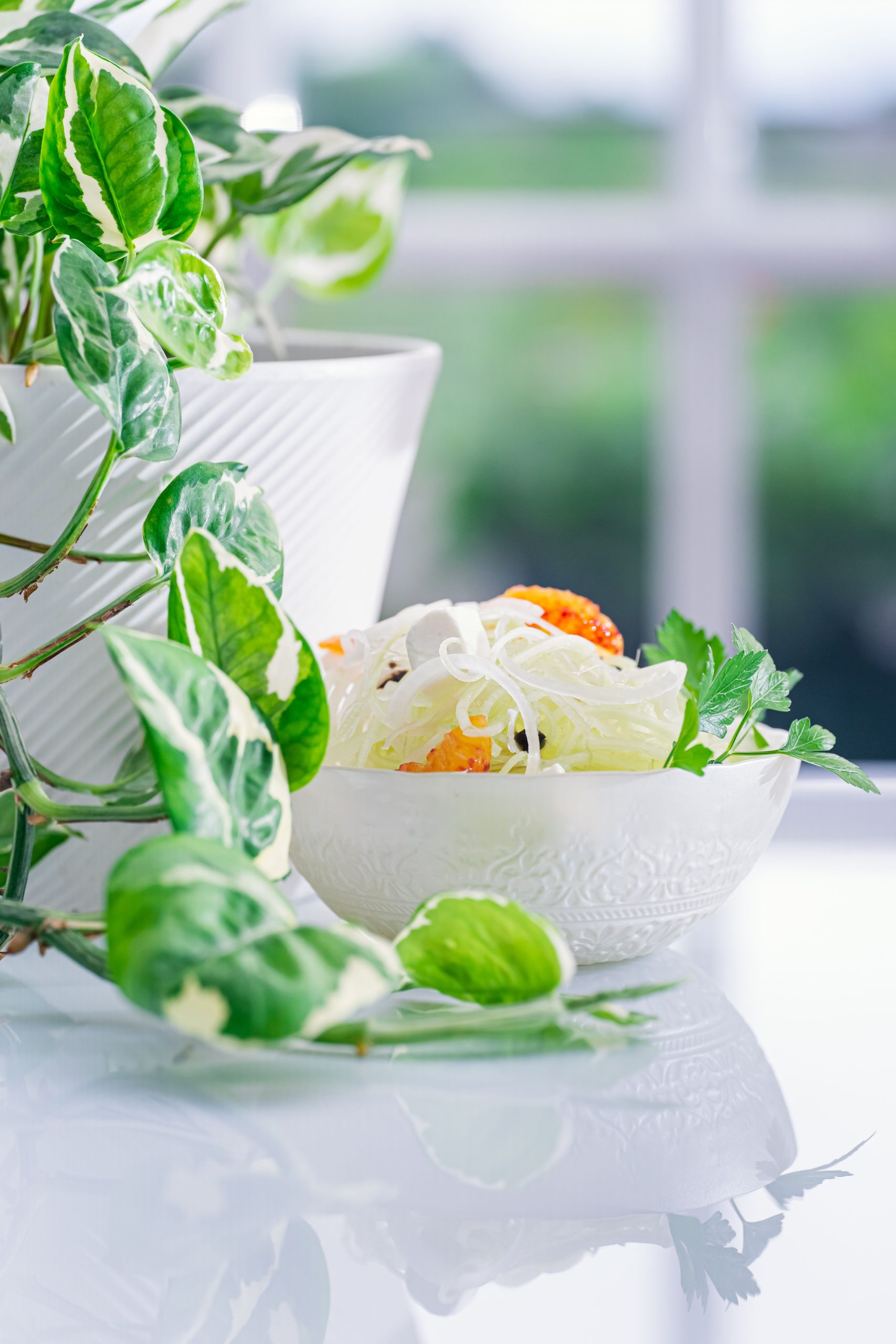 White bowl of fresh salad with greenery on reflective surface with soft daylight. Bol blanc de salade fraîche avec de la verdure sur une surface réfléchissante avec une lumière douce.