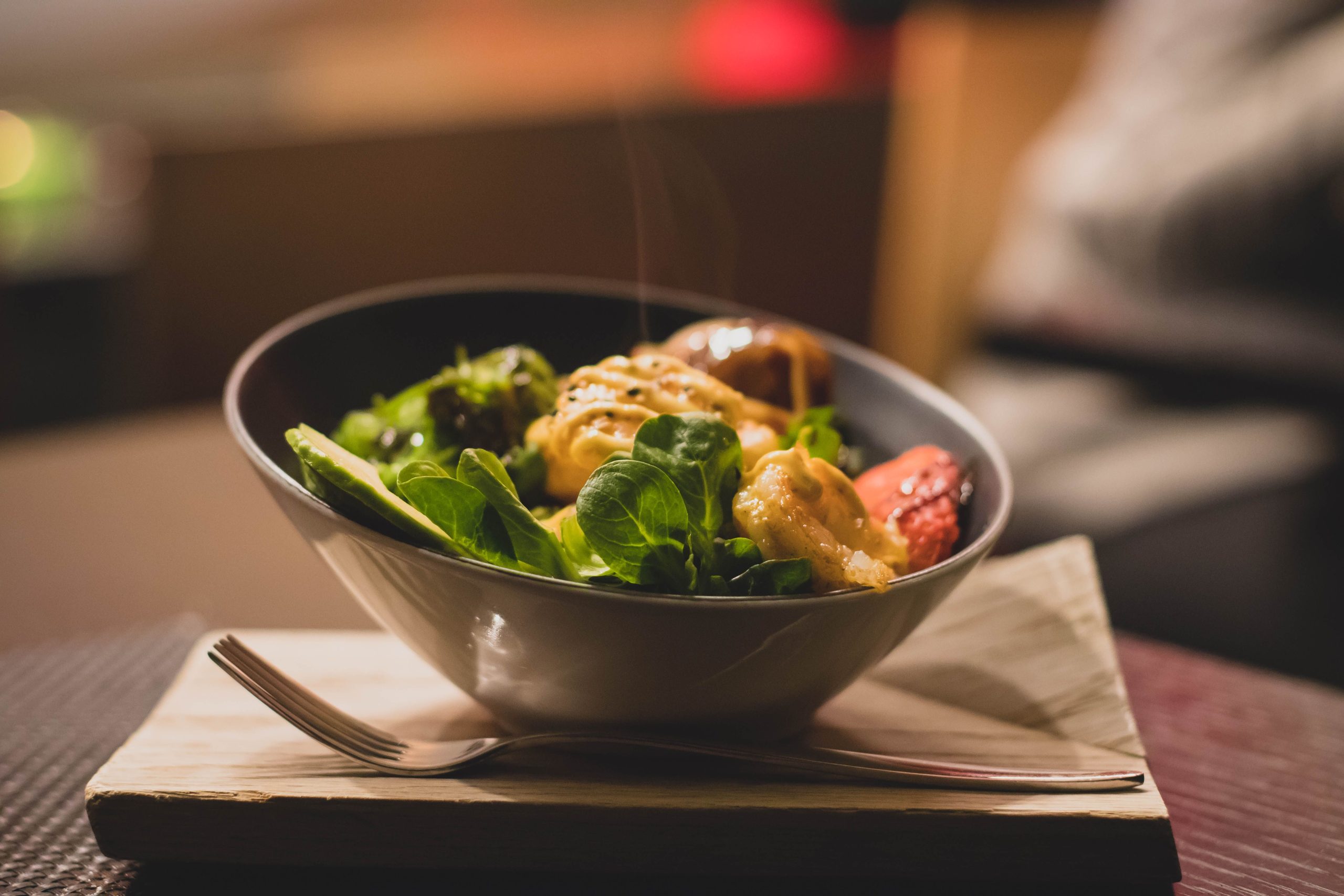 Delicious bowl of salad with fresh greens and grilled chicken served on a wooden platter. Bol délicieux de salade avec des légumes verts frais et du poulet grillé servi sur un plateau en bois.