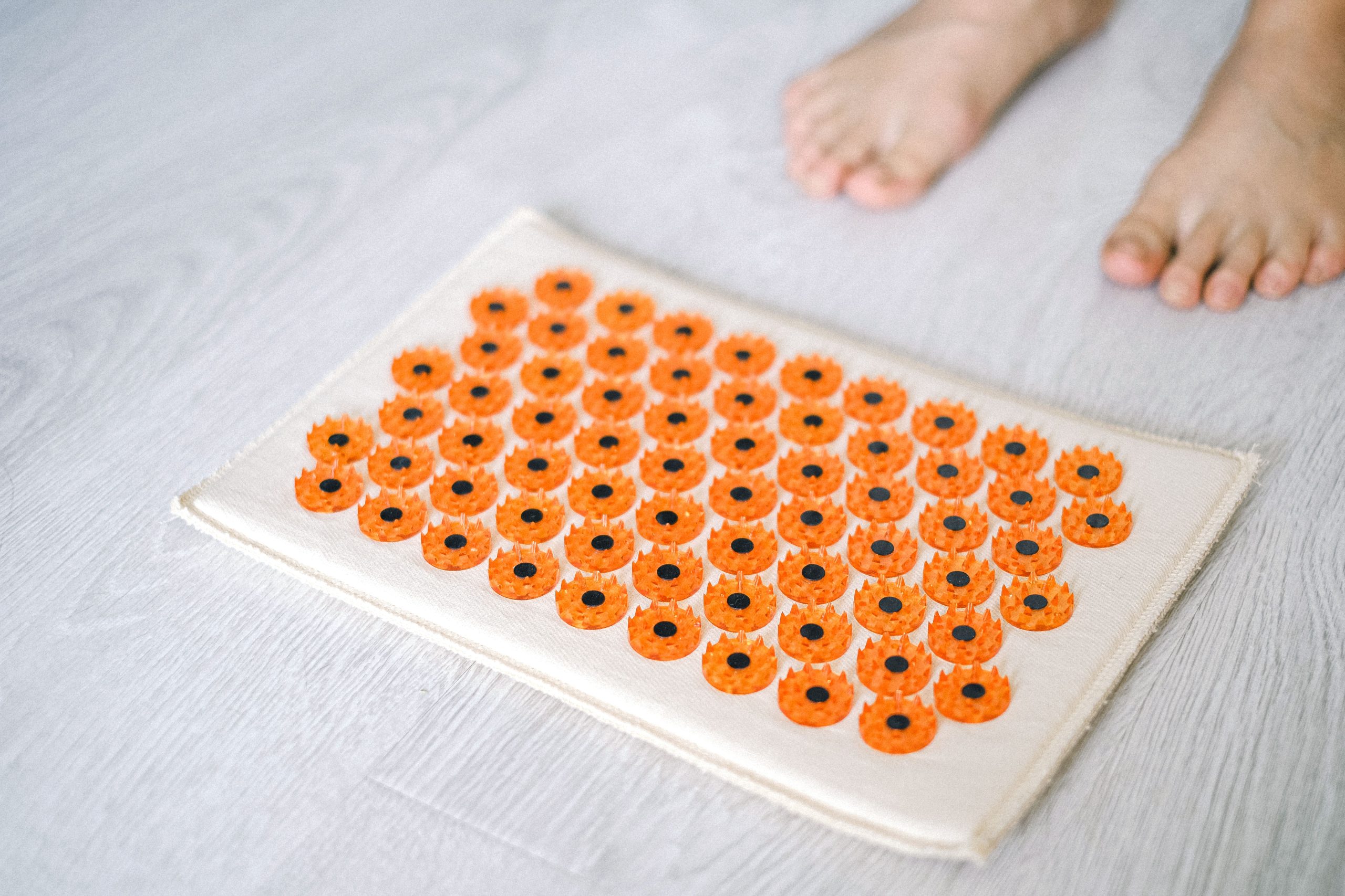 Close-up of a foot acupressure mat on a wooden floor, ideal for relaxation therapies. Gros plan d'un tapis d'acupression pour les pieds sur un plancher en bois, idéal pour les thérapies de relaxation.