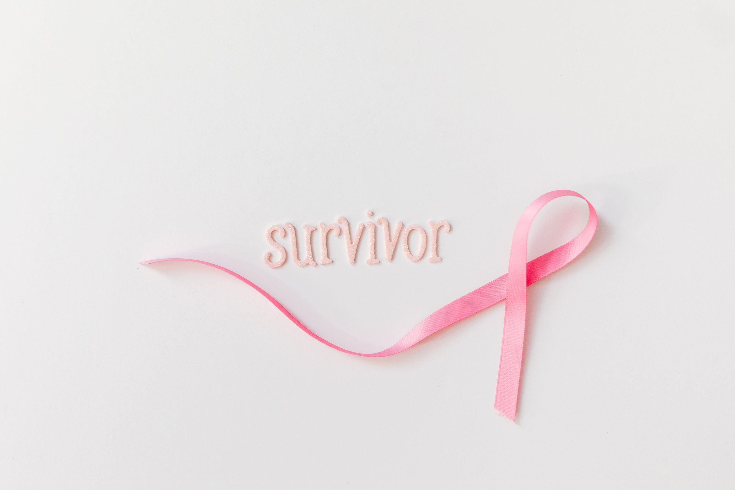 Pink ribbon next to 'survivor' text symbolizing breast cancer awareness and hope. Ruban rose à côté du texte « survivor » symbolisant la sensibilisation au cancer du sein et l'espoir.