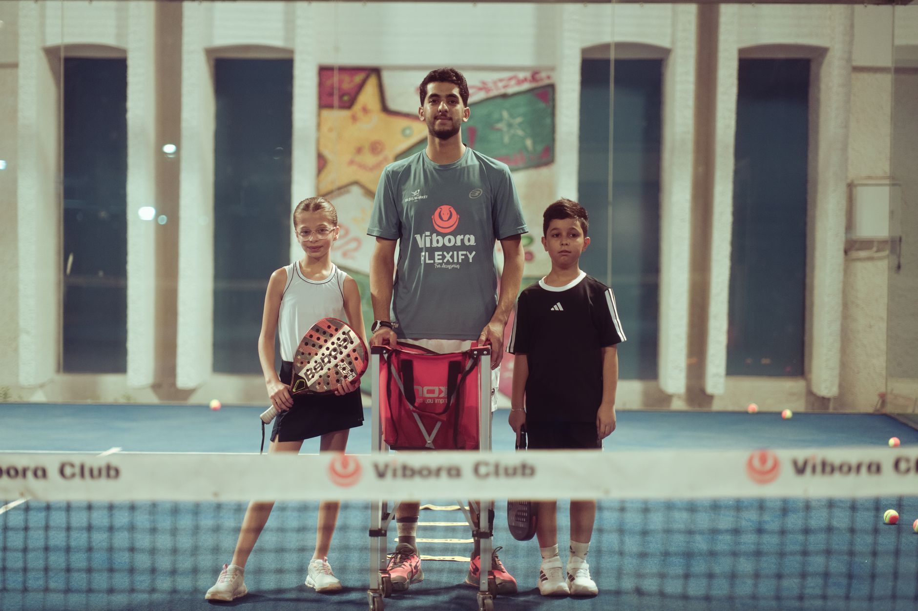 Coach de padel qui encadre deux jeunes joueurs en intérieur