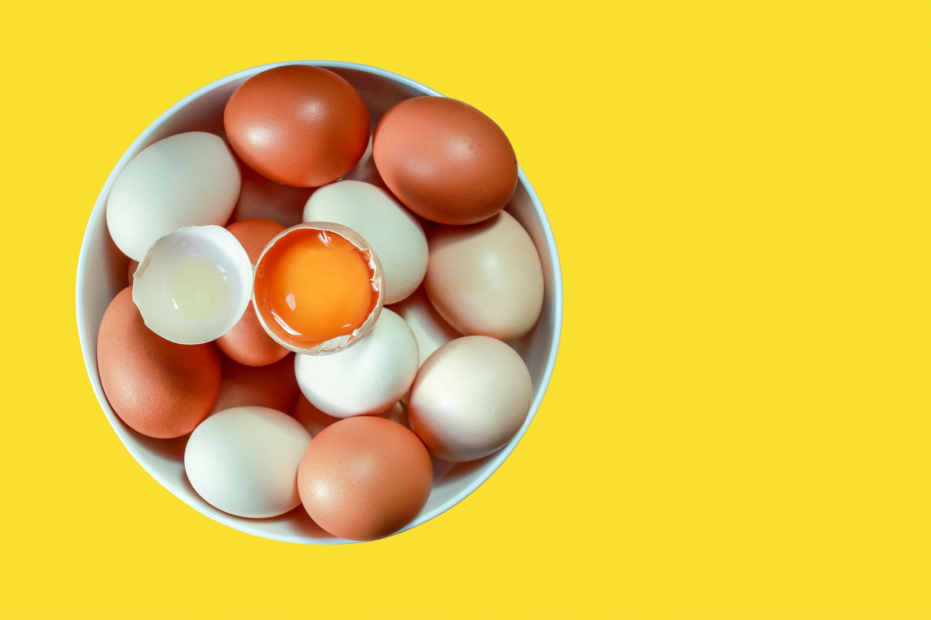 Œufs blancs et bruns dans un bol sur fond jaune